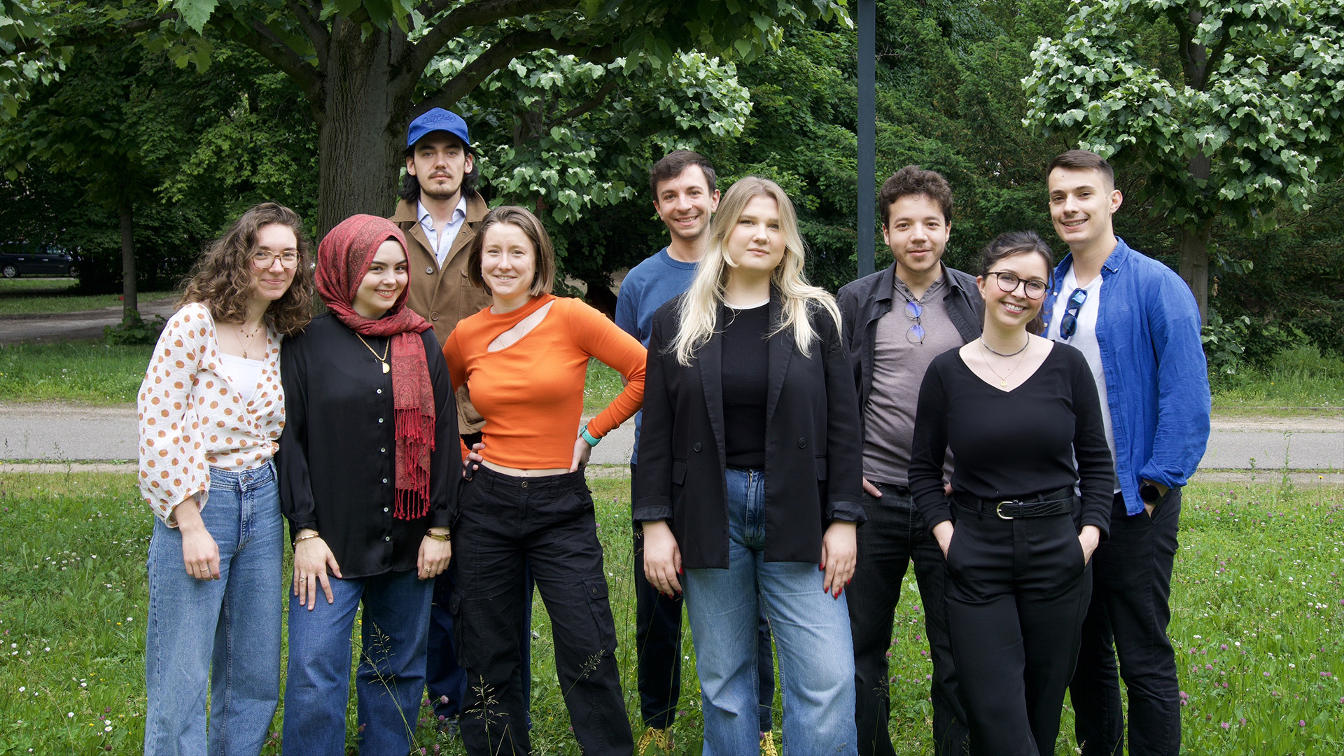 Photographie de la promotion 2022-2024 du Master Design des Environnements Numériques (MDEN), de la faculté des Arts de l'Université de Strasbourg. De gauche à droite sont visibles les étudiants de la promotion, respectivement : Clara Papot, Mélissa Toklu, Hugo Anneheim, Mélaine Marrocq, Nicolas Diebold, Natalia Palechek, Robin Roland, Lyson Rougeon, Maël Guillemot.